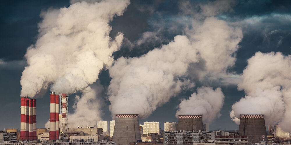 Power plant smokestacks emitting smoke over urban cityscape